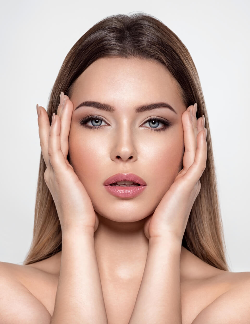 a woman with light brown long hair framing her face with her hands standing against a light background