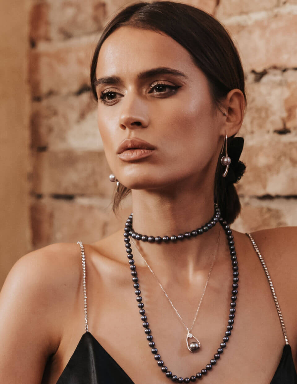 a portrait of a young woman with brown eyes and hair pulled back, wearing black pearl necklace and long silver earrings