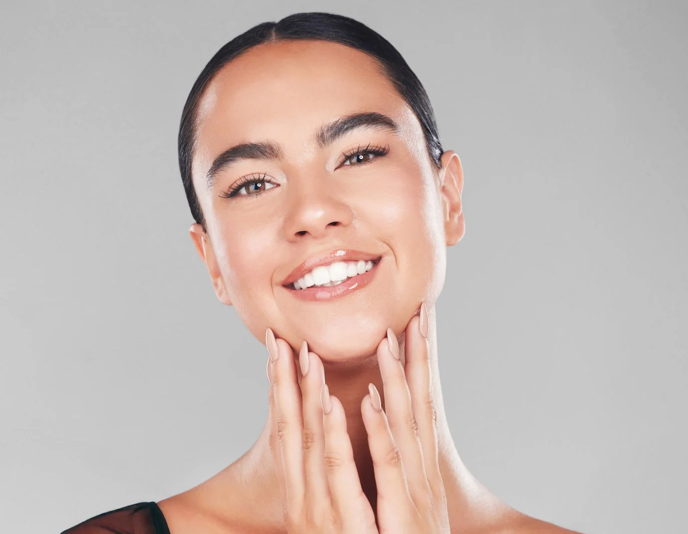 a woman with dark brown hair in a bun standing against a light grey background