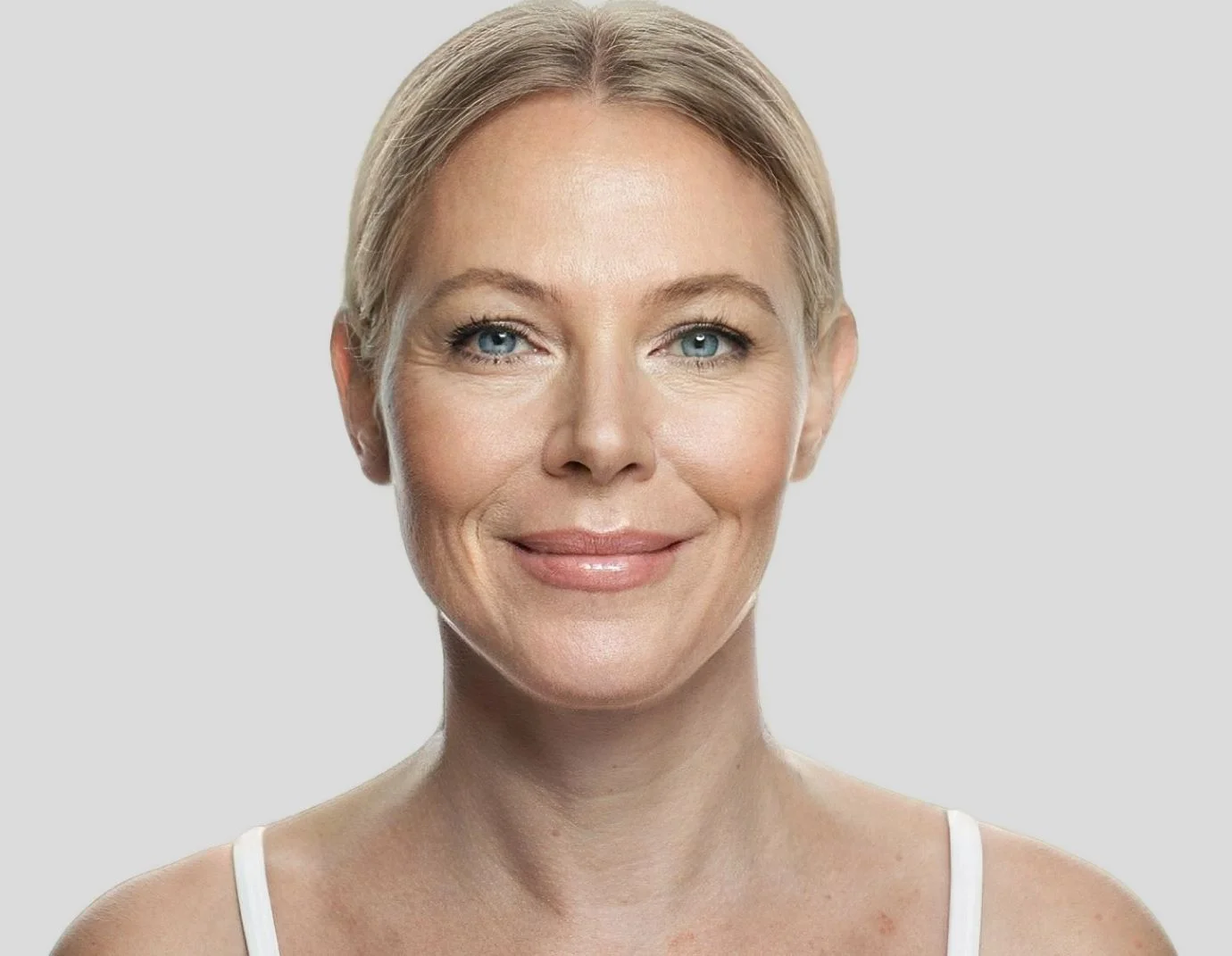a mature blond woman with her hair pulled back standing against a light grey background