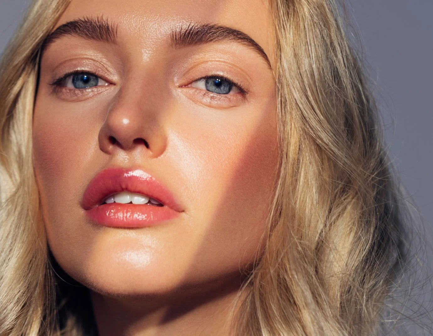 a closeup of a young woman with long blonde hair against a blue grey background